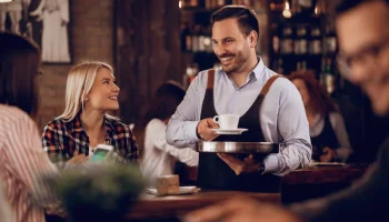 happy-waiter-communicating-with-customers-while-serving-them-coffee-pub_637285-2437