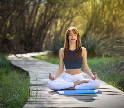 Young woman doing yoga in nature. Female wearing sport clothes in lotus figure. Girl sitting on wooden road.